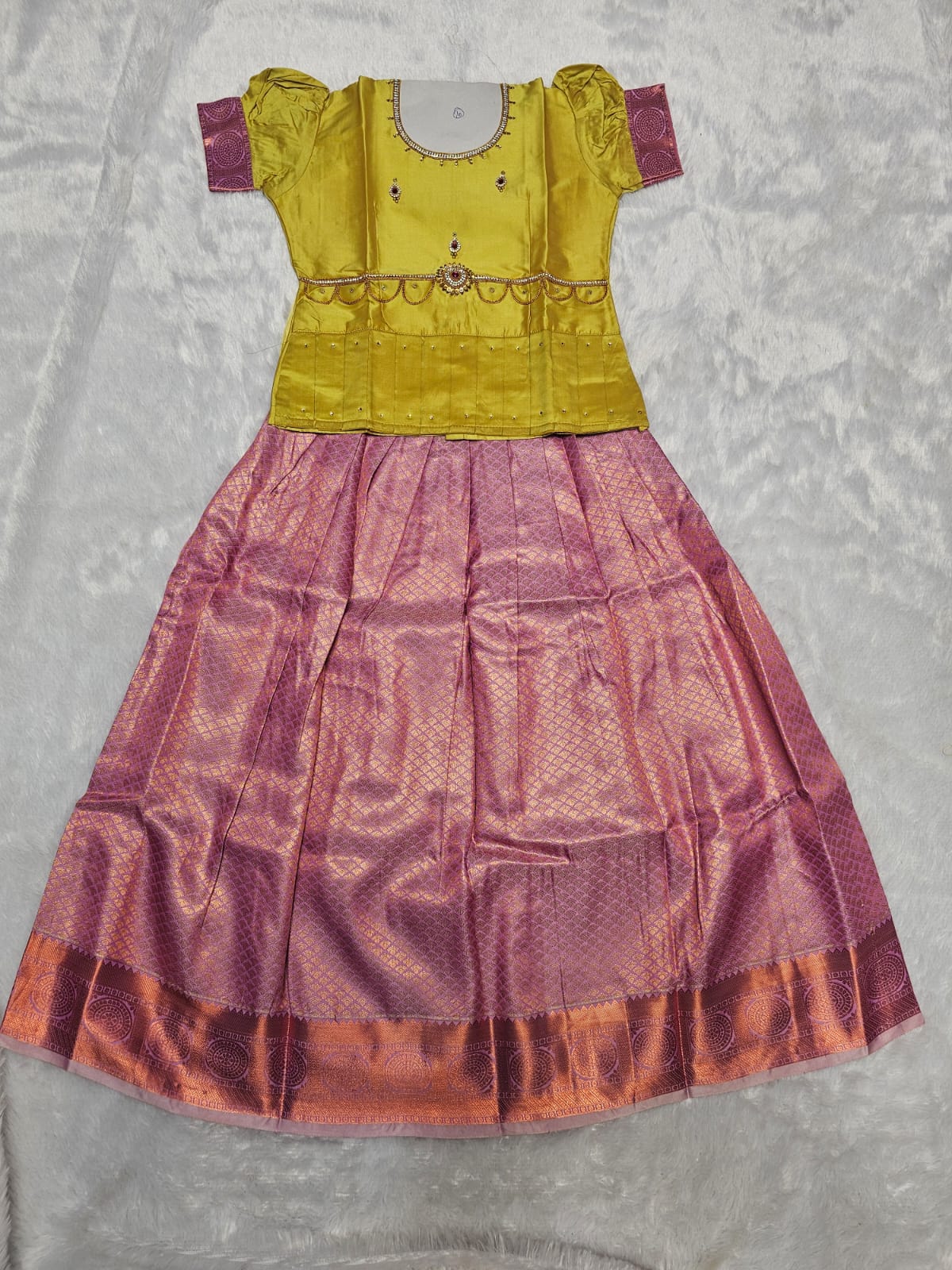 Mustard yellow semi silk top with lavender purple bridal silk skirt pattu pavadai for girls featuring puff sleeves, waist belt detailing and double chain stone neck work by Sri Thulir Tex