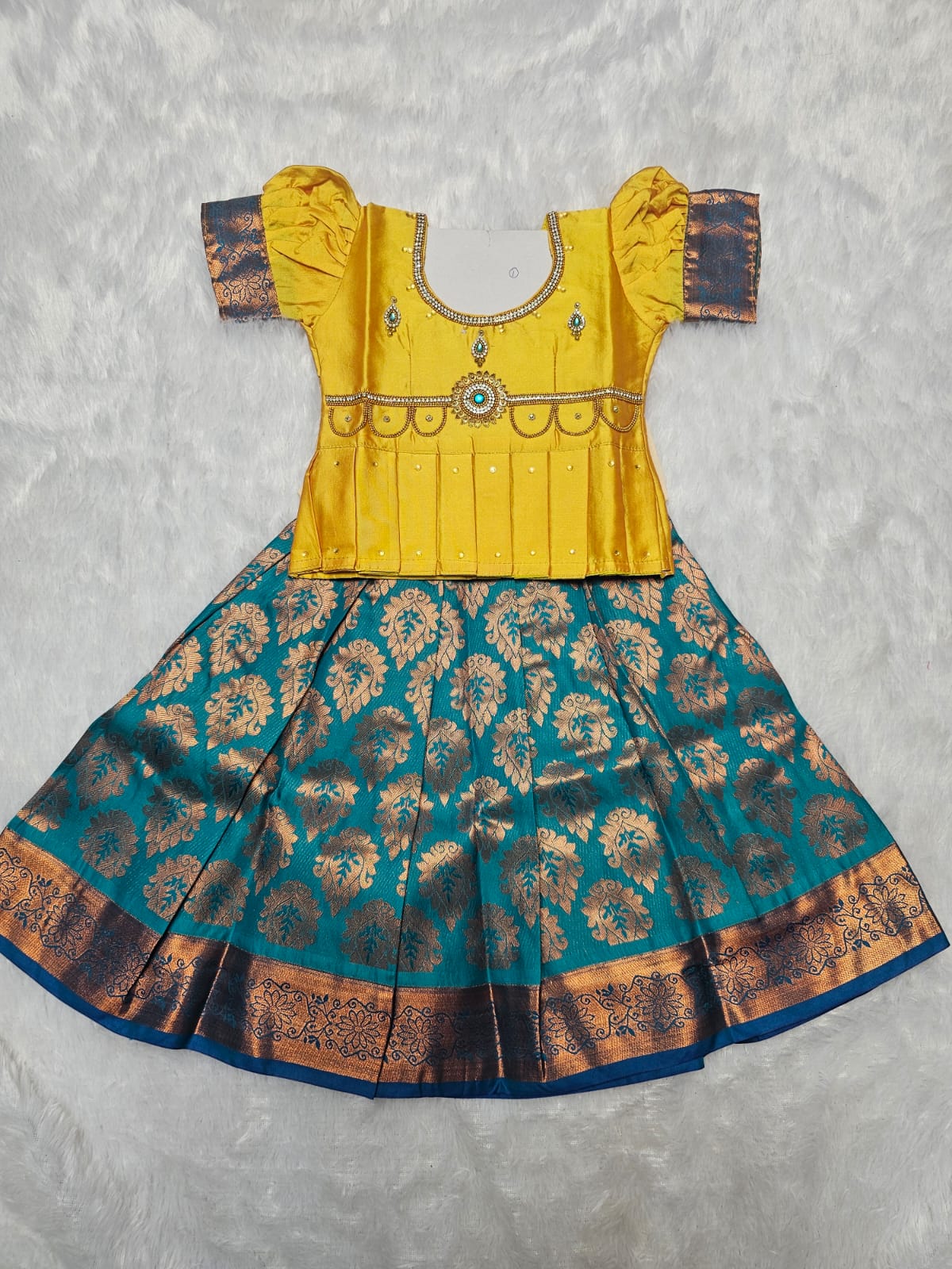 Mustard yellow semi silk blouse with teal blue bridal silk skirt pattu pavadai for girls featuring puff sleeves, waist belt design and double chain neck stone work