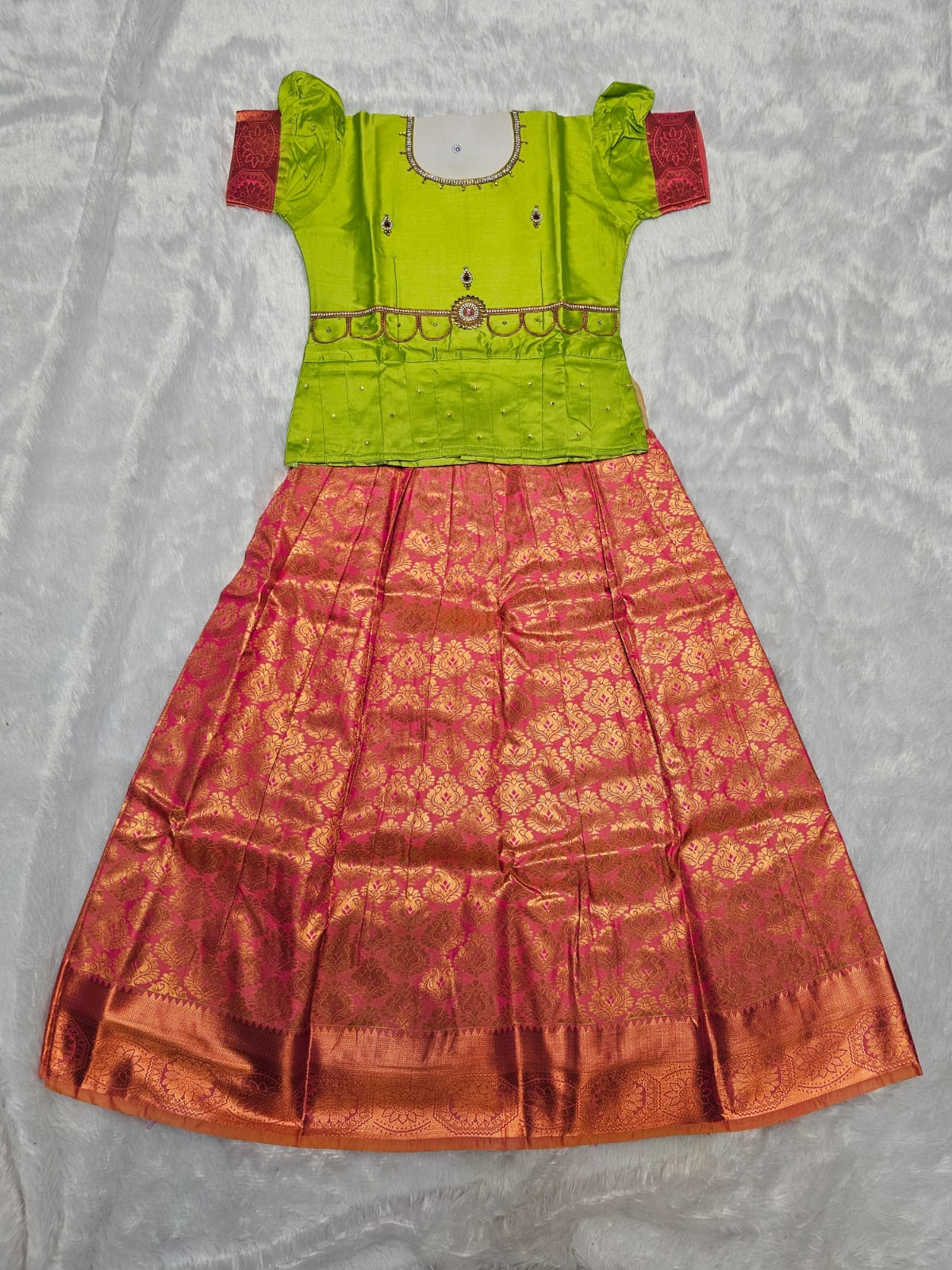 Parrot green semi silk top with rani pink bridal silk skirt pattu pavadai for girls featuring puff sleeves, waist belt detailing and double chain stone neck work by Sri Thulir Tex