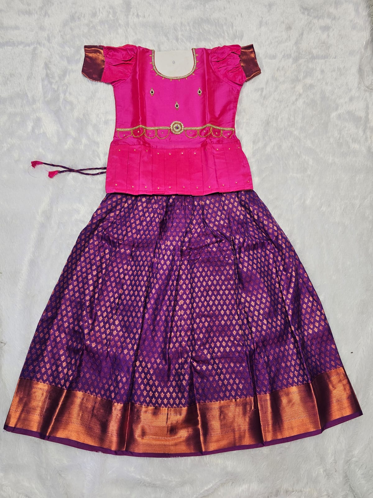 Pink semi silk top with purple bridal silk skirt pattu pavadai for girls featuring puff hand sleeves, waist belt design and double chain neck stone work by Sri Thulir Tex