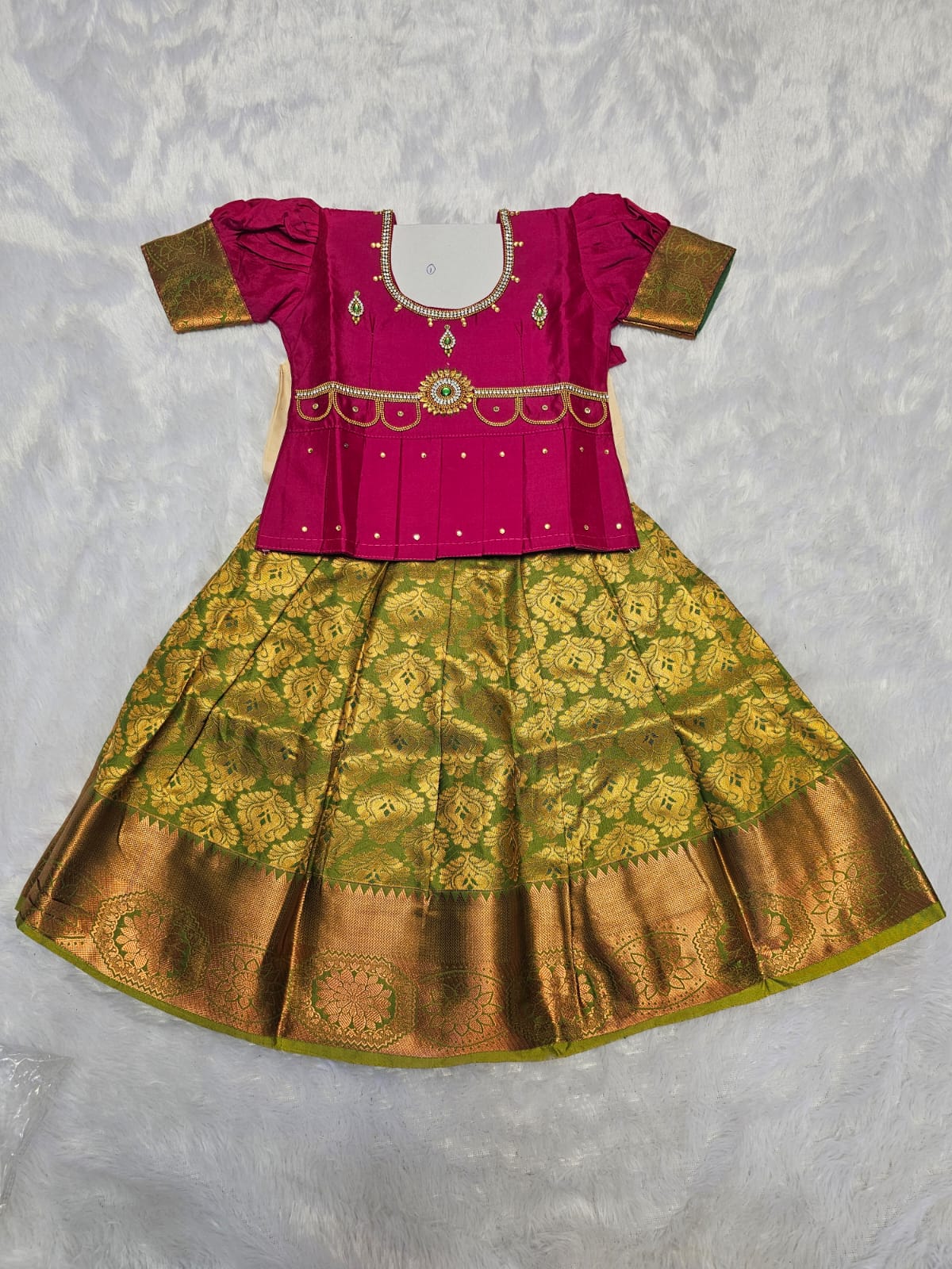Rani pink semi silk top with green bridal silk skirt pattu pavadai for girls featuring puff hand sleeves, waist belt design and double chain stone neck work by Sri Thulir Tex