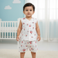 Smiling baby wearing a white multi printed muslin jabla shirt and shorts set, standing outdoors in a garden.