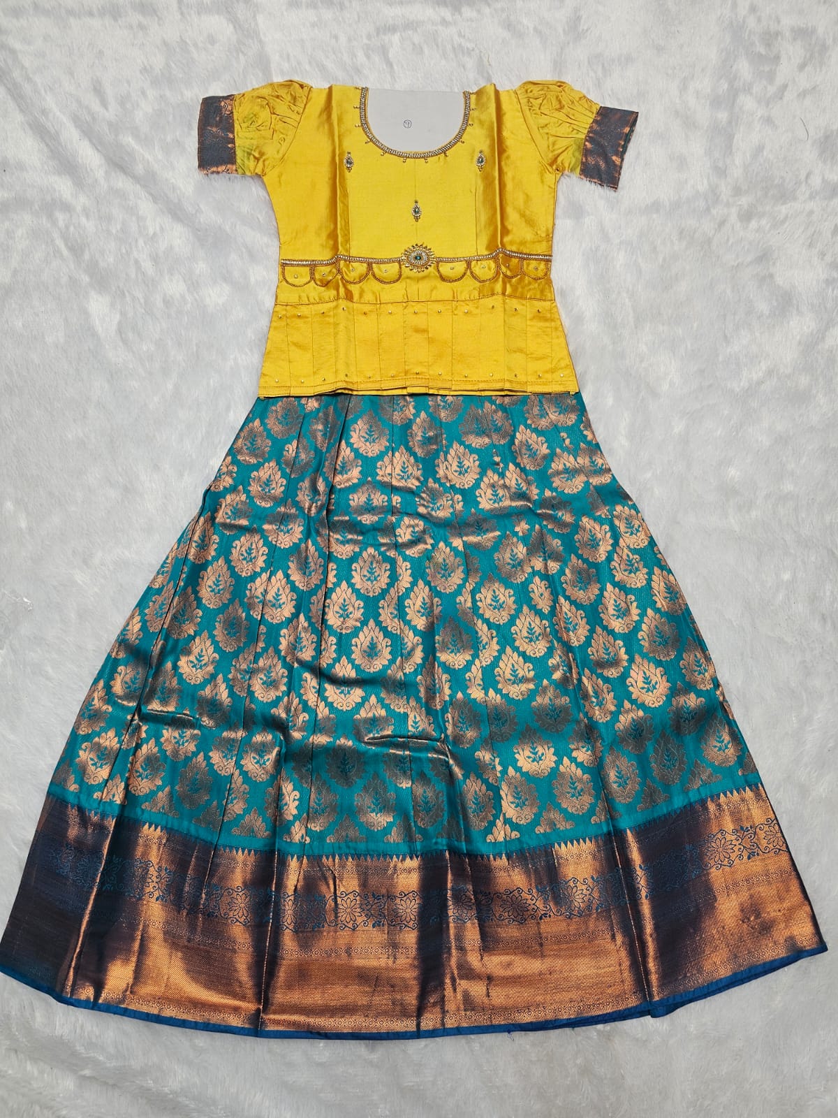 Bright yellow semi silk blouse with teal blue bridal silk skirt pattu pavadai for girls featuring puff sleeves, waist belt design and double chain neck stone work