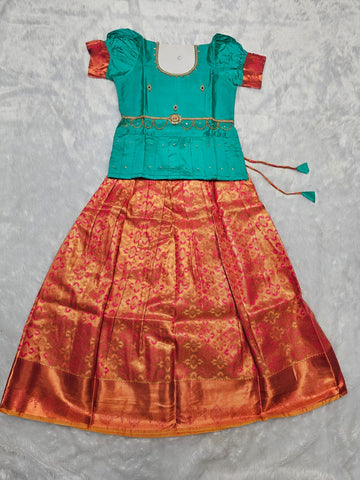 Emerald green semi silk blouse with rani pink bridal silk skirt pattu pavadai for girls featuring puff sleeves, zari border and stone work waist belt