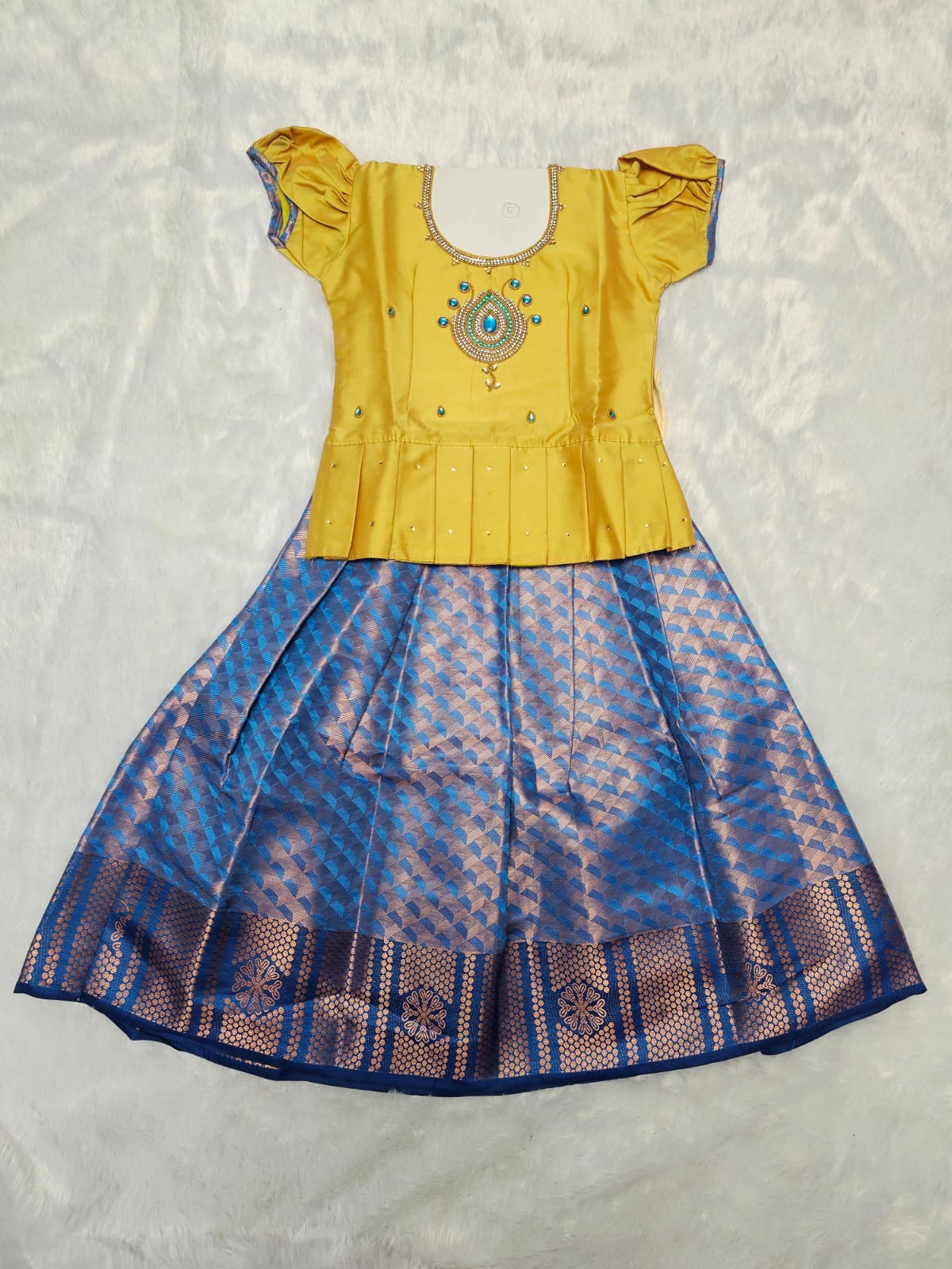 Golden yellow semi silk top with royal blue bridal silk skirt pattu pavadai for girls featuring puff sleeves and double chain stone neck work, traditional South Indian ethnic wear by Sri Thulir Tex