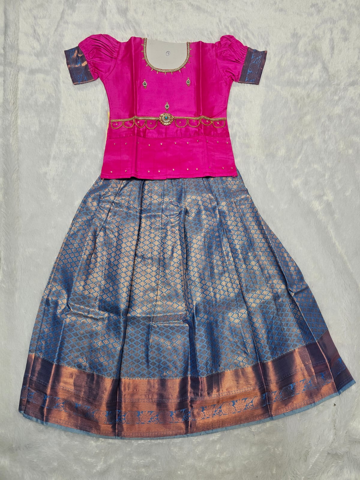 Hot pink semi silk top with steel blue bridal silk skirt pattu pavadai for girls featuring puff hand sleeves, waist belt detailing and double chain neck stone work by Sri Thulir Tex