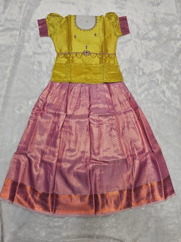 Mustard yellow semi silk top with lavender purple bridal silk skirt pattu pavadai for girls featuring puff sleeves, waist belt detailing and double chain stone neck work by Sri Thulir Tex