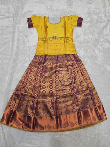 Mustard yellow semi silk top with purple bridal silk skirt pattu pavadai for girls featuring puff sleeves, waist belt detailing and double chain stone neck work by Sri Thulir Tex