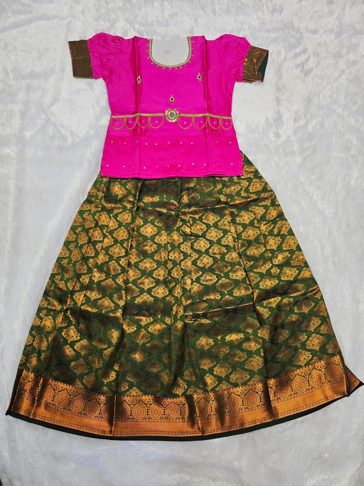 Pink semi silk top with green bridal silk skirt pattu pavadai for girls featuring puff hand sleeves, waist belt design and double chain neck stone work by Sri Thulir Tex