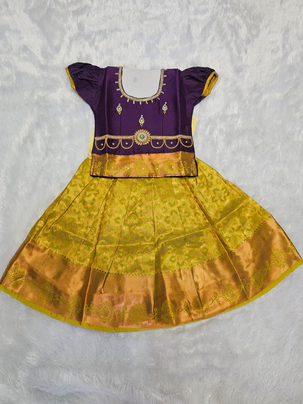 Purple semi silk top with green bridal silk skirt pattu pavadai for girls featuring puff hand sleeves, waist belt detailing and double chain stone neck stone work by Sri Thulir Tex