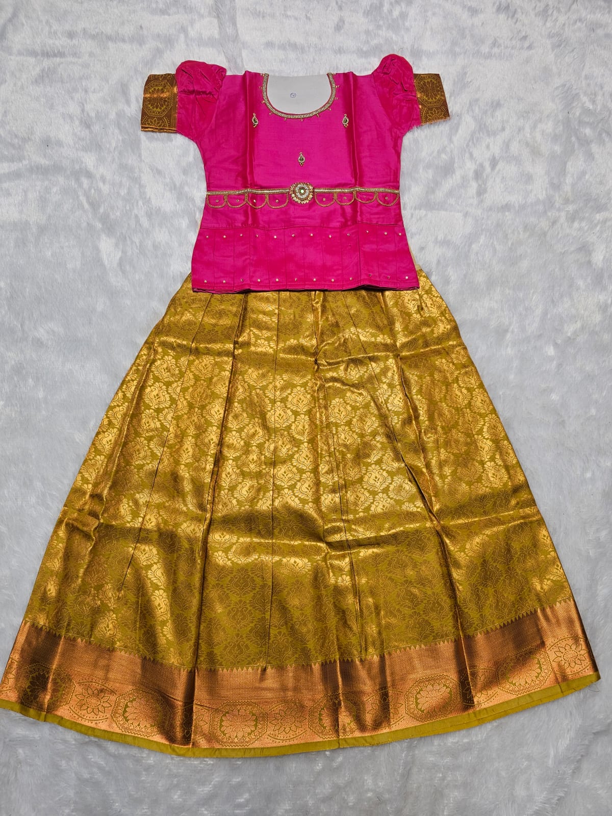 Rani pink semi silk blouse with antique gold bridal silk skirt pattu pavadai for girls featuring zari border, puff sleeves and stone work waist belt