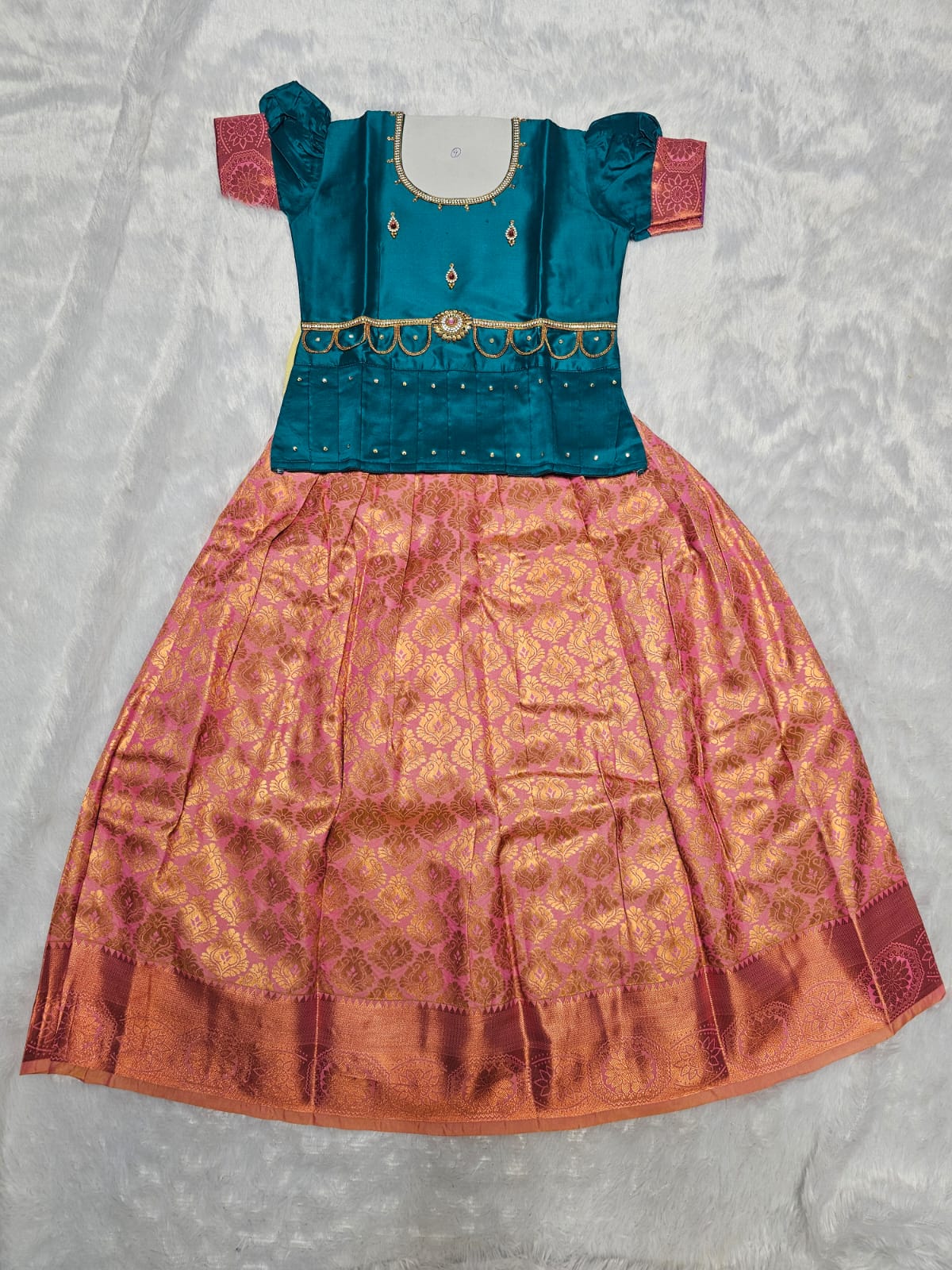 Teal blue semi silk top with rose pink bridal silk skirt pattu pavadai for girls featuring puff sleeves, waist belt detailing and double chain stone neck work by Sri Thulir Tex