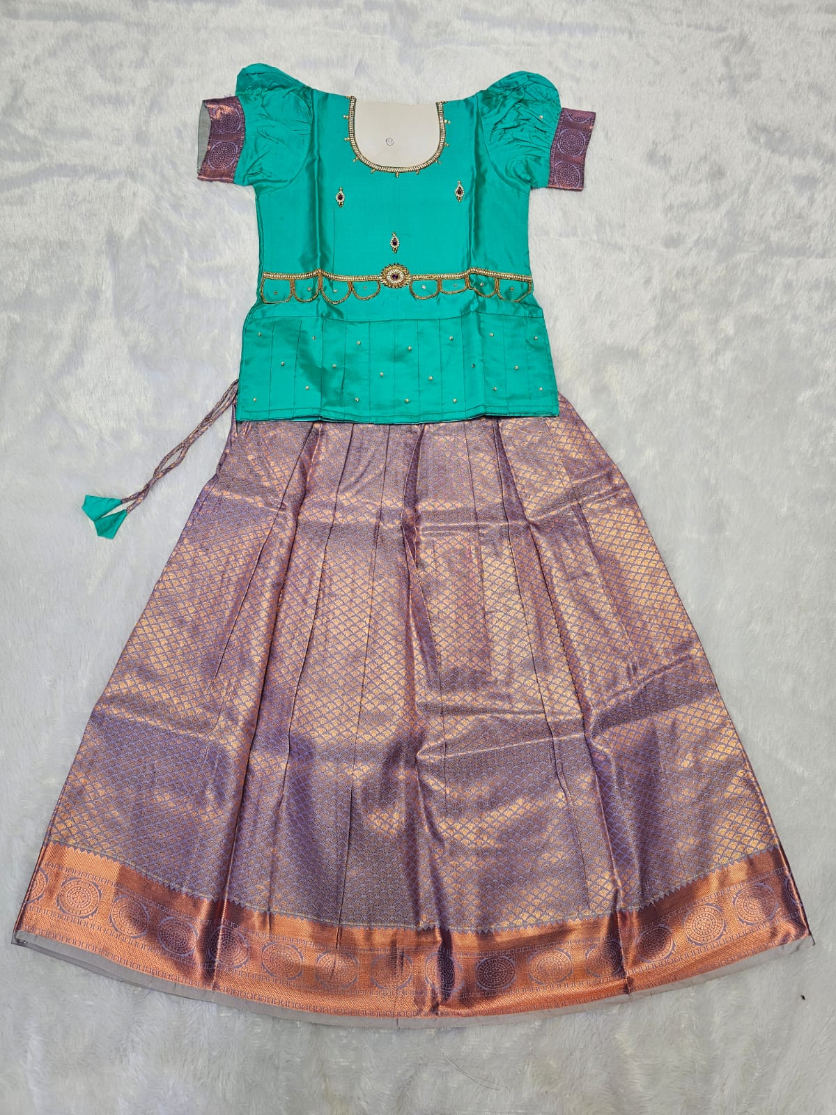 Teal green semi silk top with lavender bridal silk skirt pattu pavadai for girls featuring puff hand sleeves, waist belt design and double chain neck stone work by Sri Thulir Tex