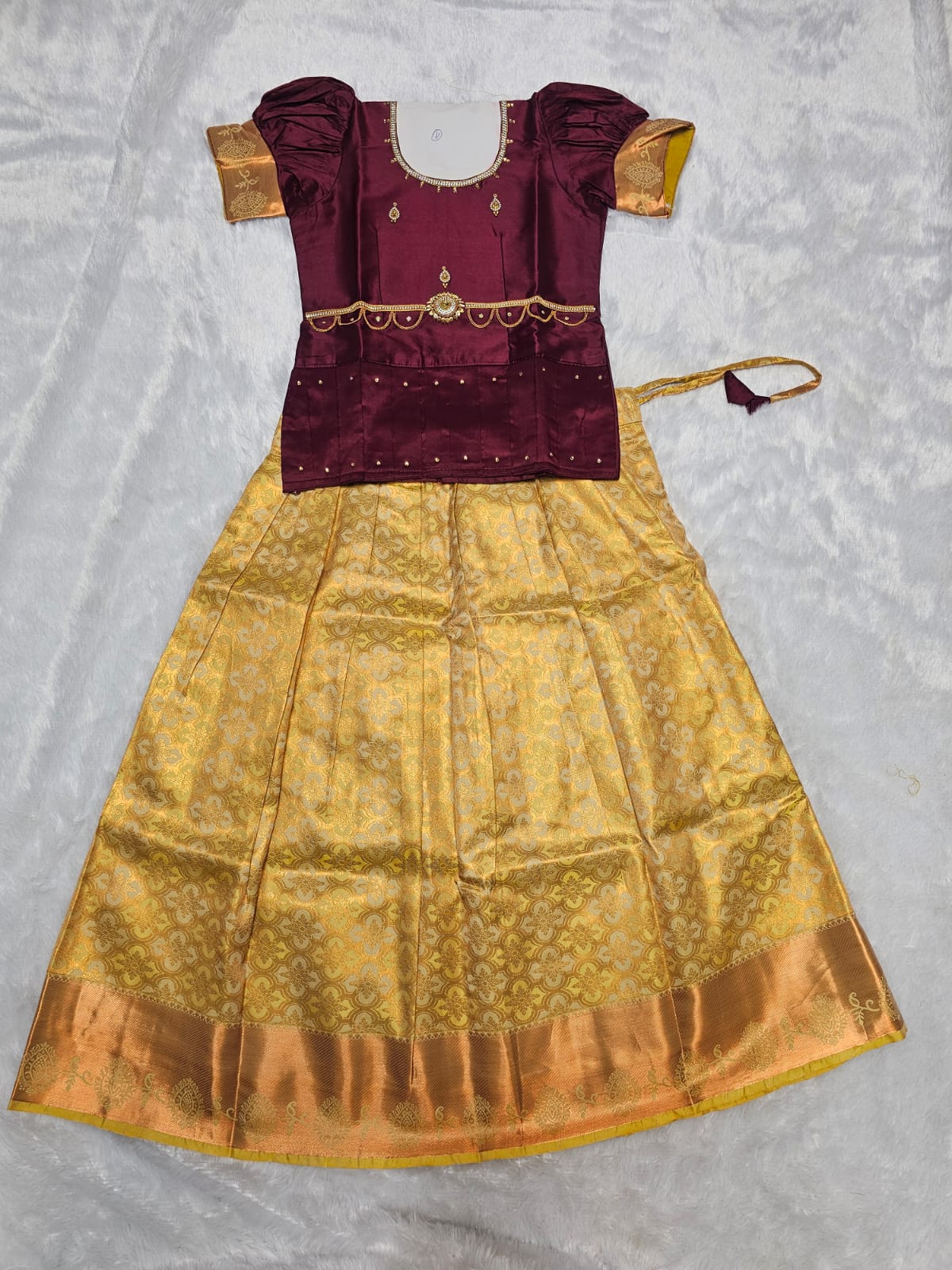 Wine maroon semi silk top with gold bridal silk skirt pattu pavadai for girls featuring puff sleeves, waist belt detailing and double chain stone neck work by Sri Thulir Tex
